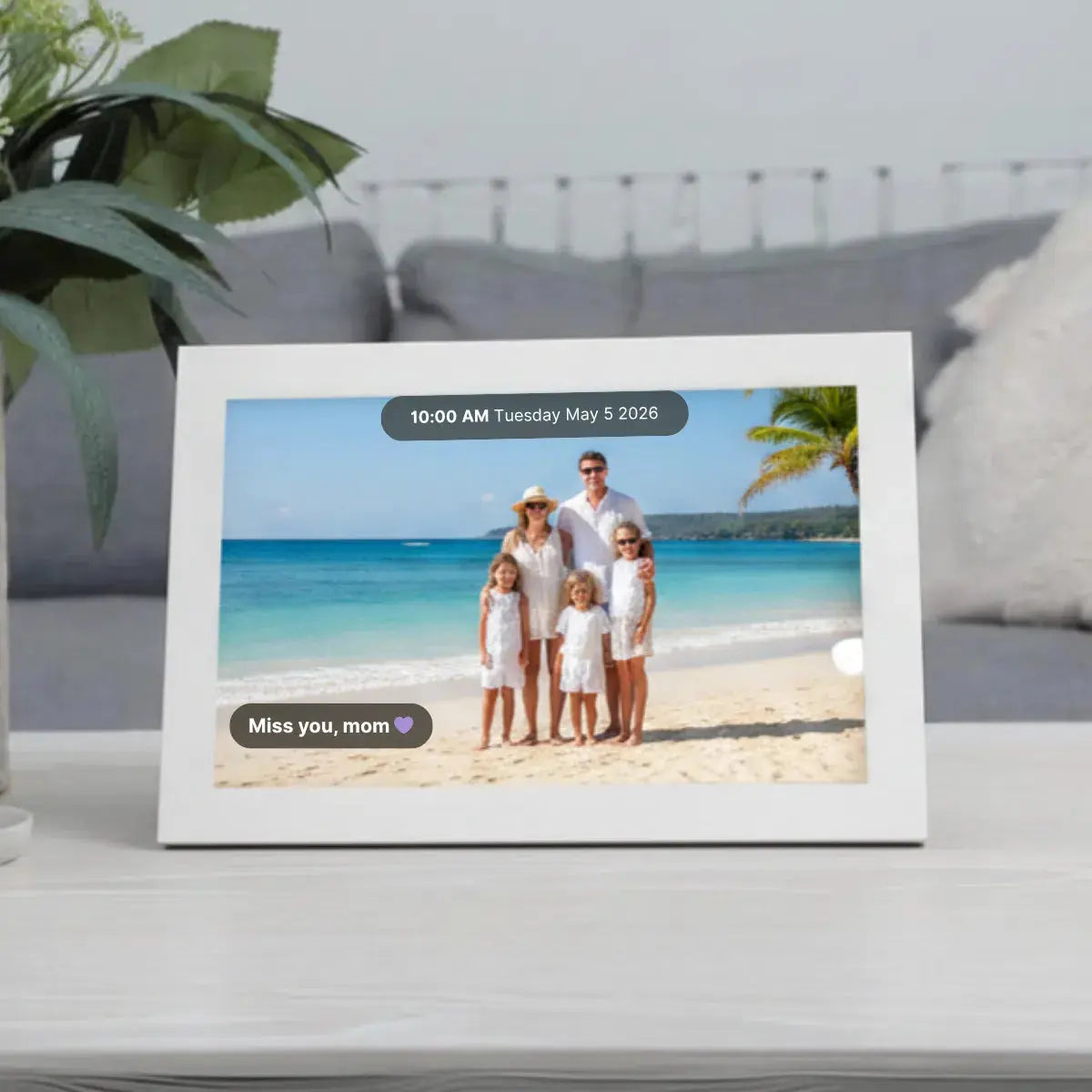 Memoryboard digital display on a table showing a family beach photo with the message “Miss you, mom” and the date and time at the top.
