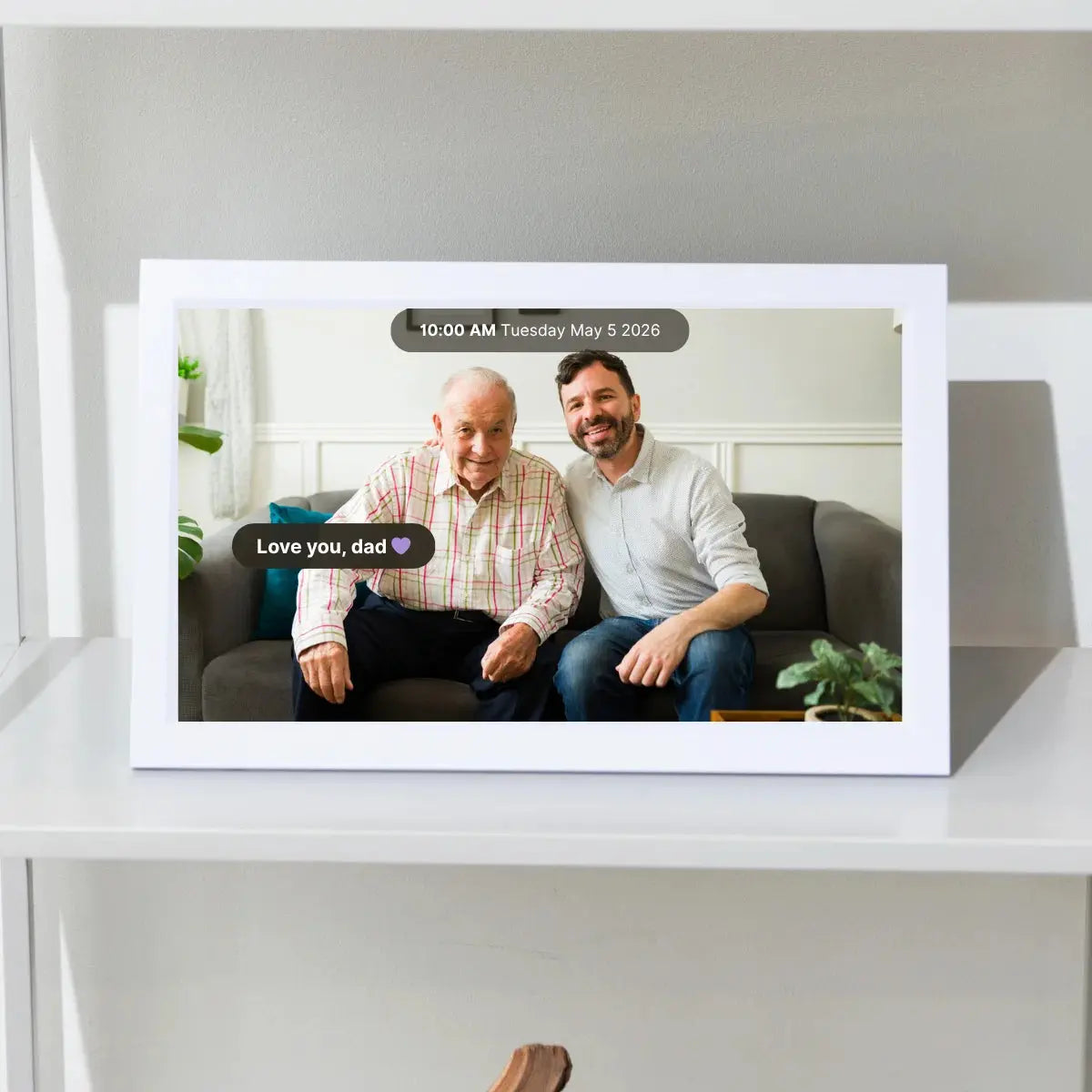 Memoryboard digital display on a shelf showing a photo of a father and son with the message “Love you, dad” and the date and time at the top.